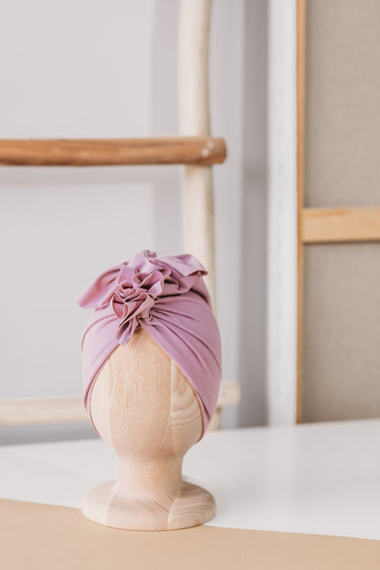 a pink turban on a wooden mannequin with wooden rack and white wall in the  background