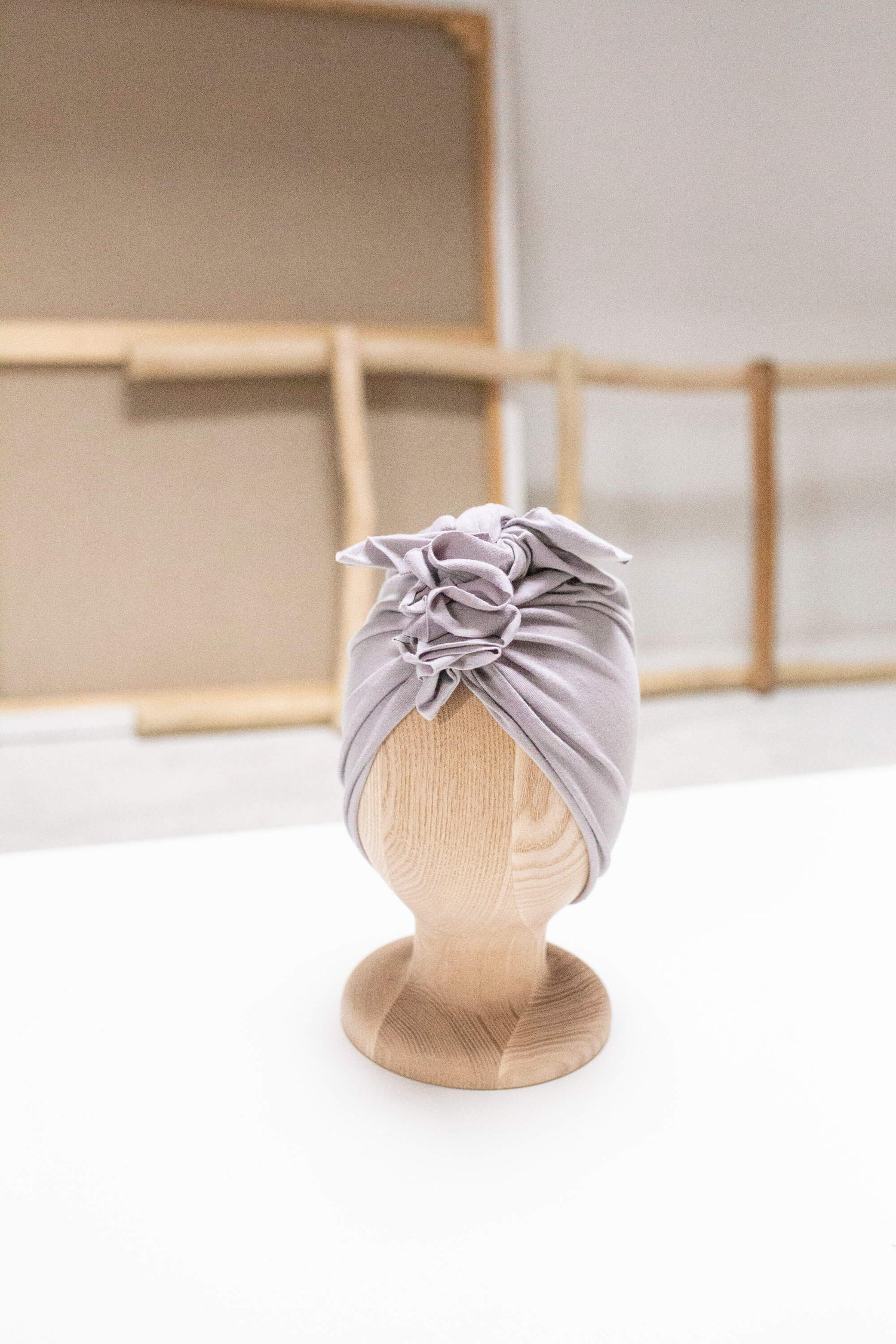 a grey baby and toddler turban on a wooden mannequin on a background with wooden rack and beige white wall