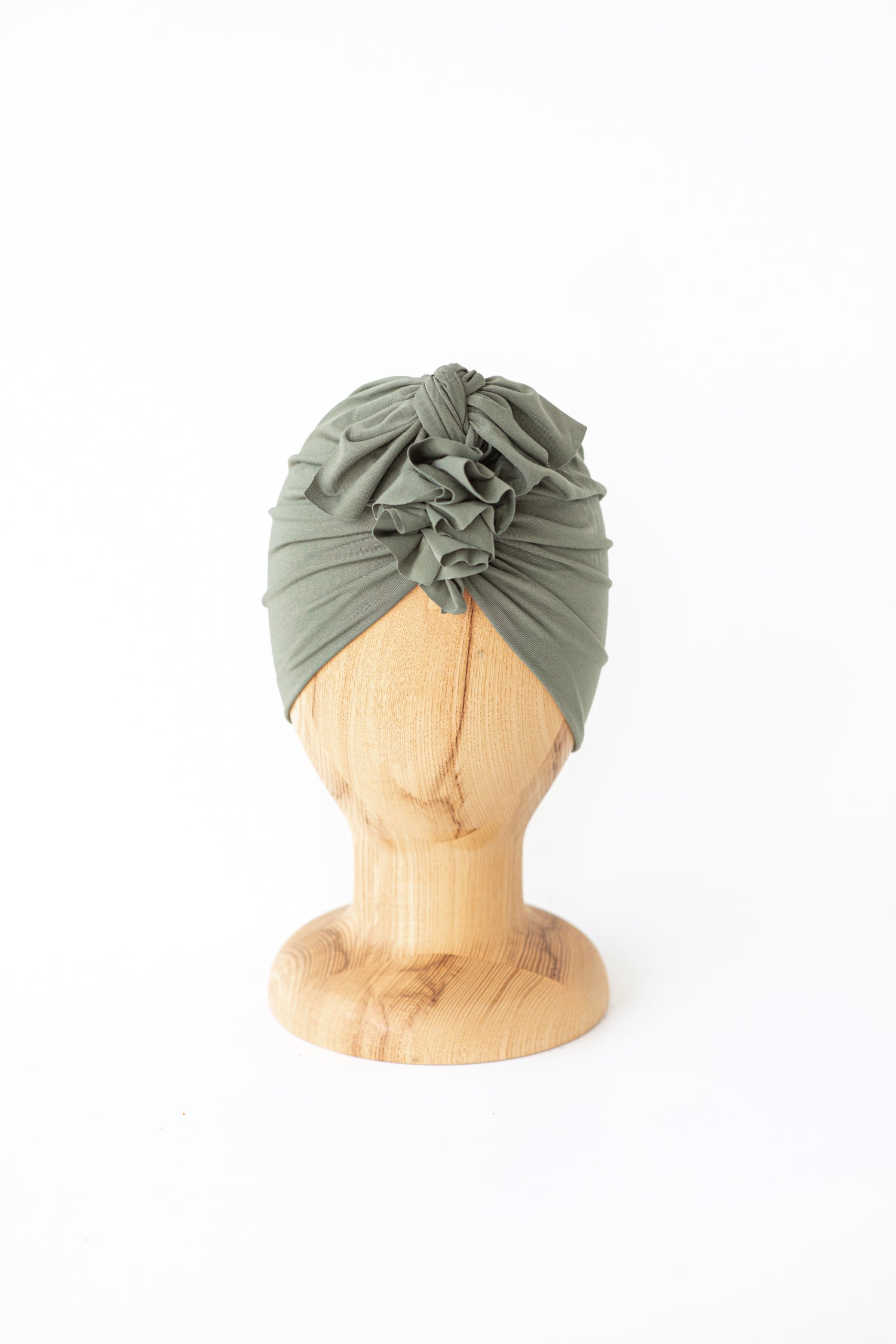 baby turban in color sage green on a wooden head mannequin on a white background