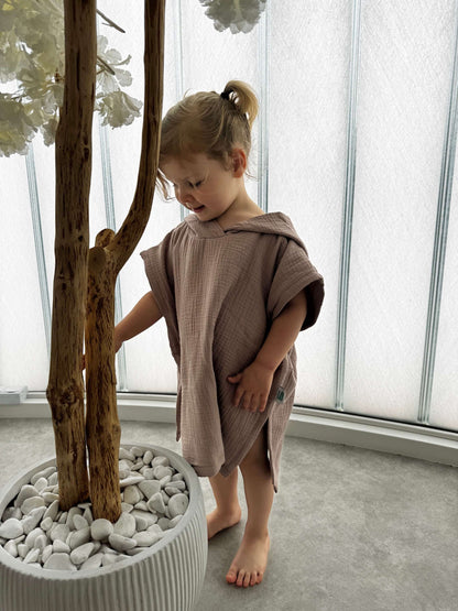 Child in a brown towel standing next to a potted plant indoors
