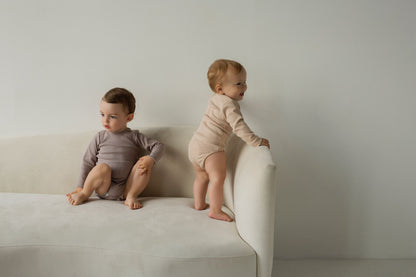 two babies on the couch wearing beige bodysuits