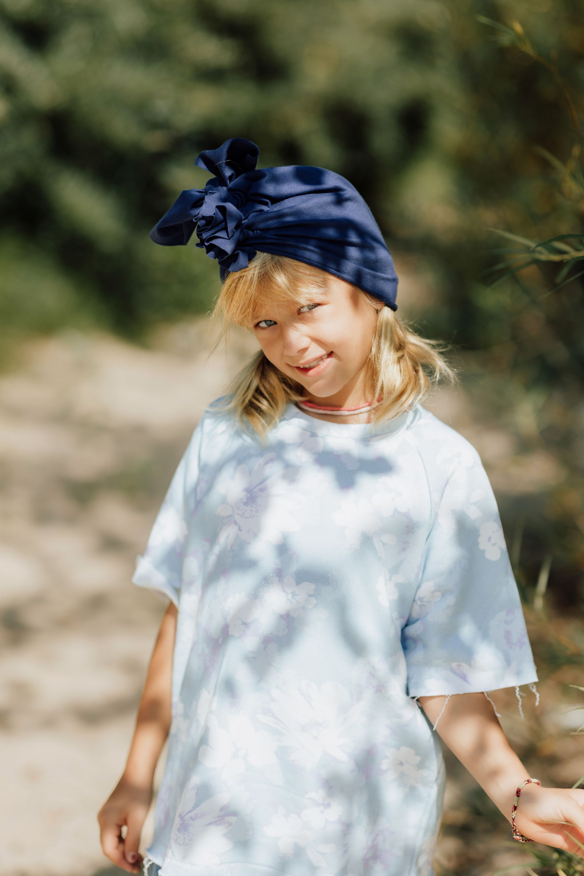 A girl smiling and wearing navy blue turnban and light blue tshirt on a green backdrop