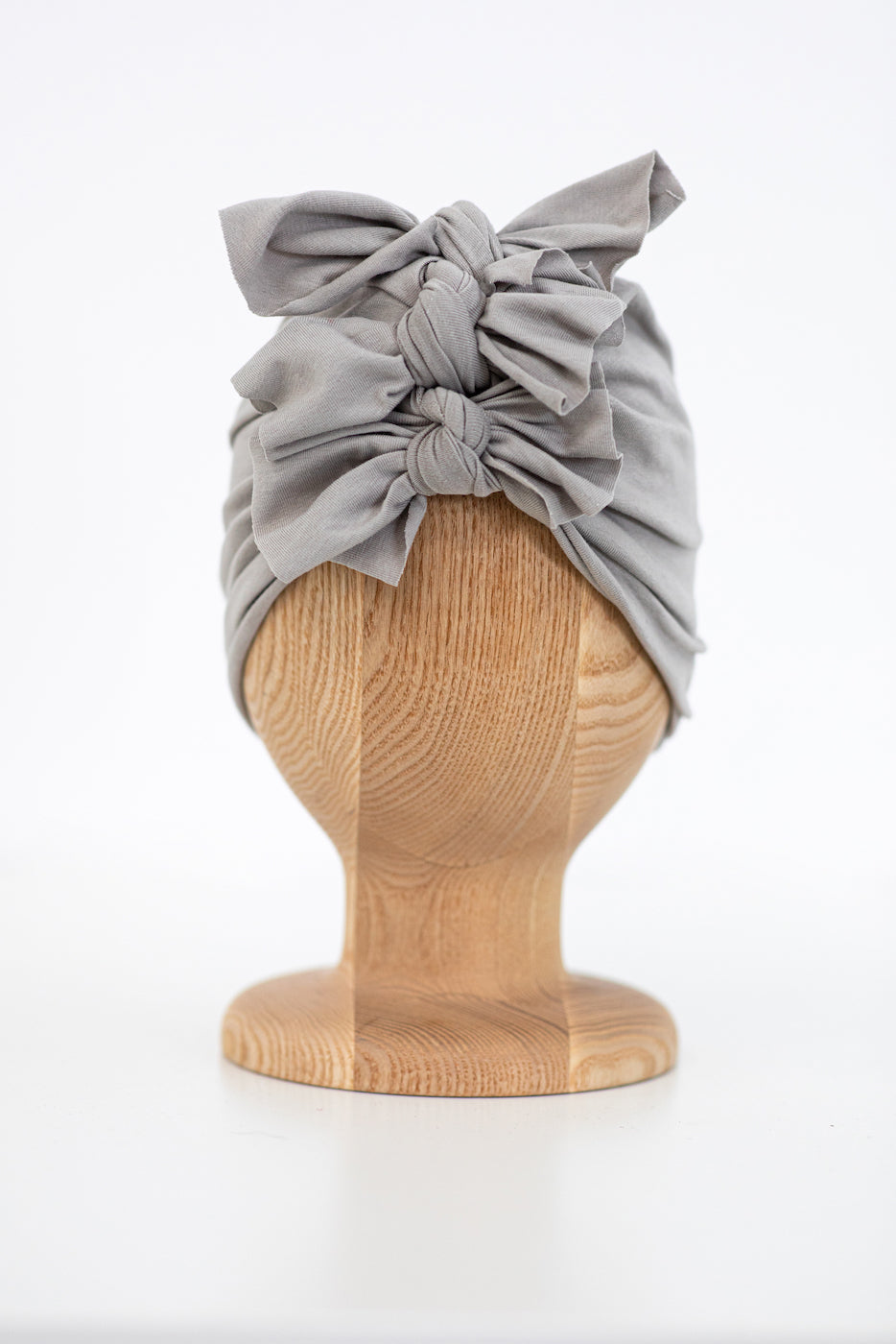 a grey baby and toddler turban on a wooden mannequin with a white plain background