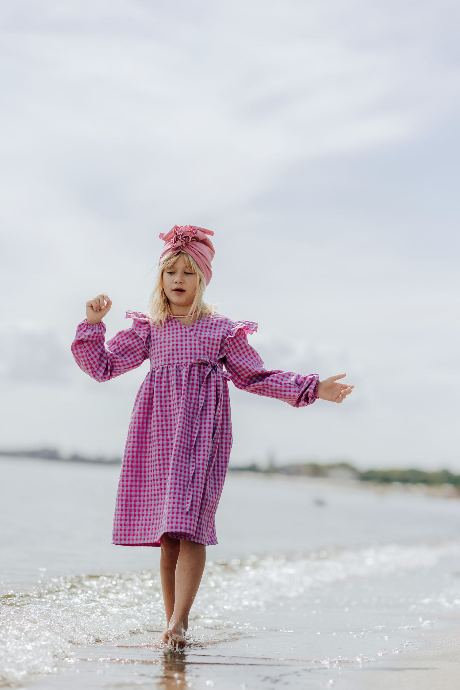 6 year old girl walking on the beach close to the water and wearing a pink purple dress and a pink girl turban