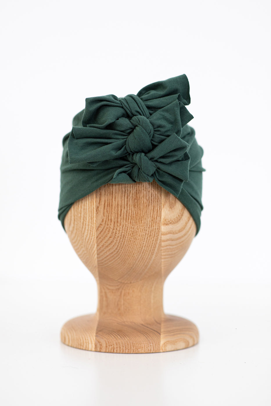 a dark green organic cotton baby turban on a wooden mannequin with white background