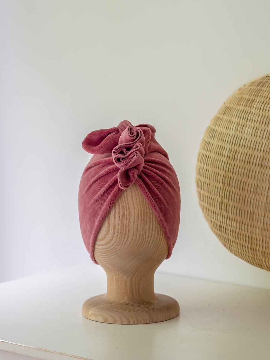 baby turban in color dusty pink on a wooden head mannequin with round rattan decoration in the background