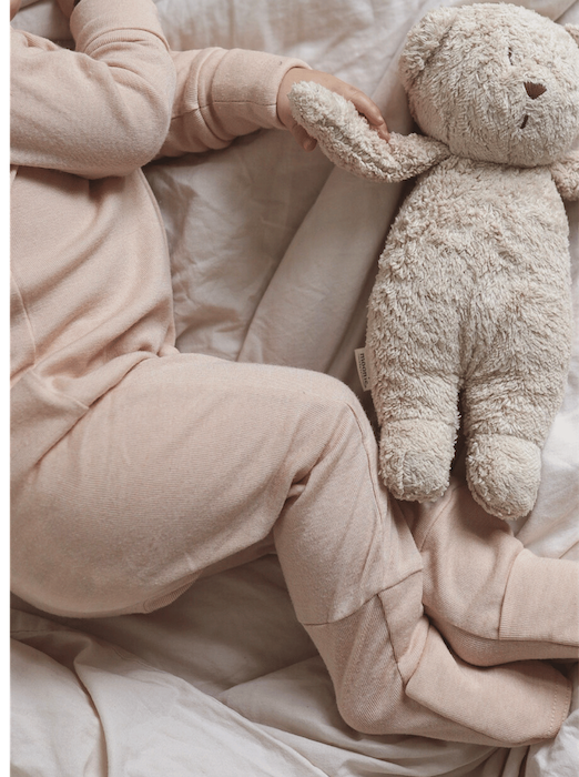 sleeping baby wearing beige overall made from merino wool and silk holding a teddy bear