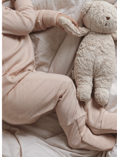 sleeping baby wearing beige overall made from merino wool and silk holding a teddy bear