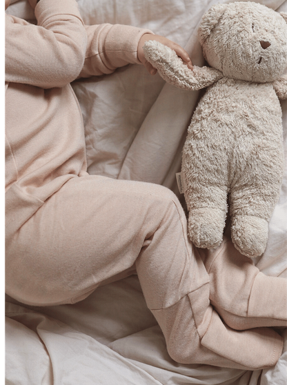 sleeping baby wearing beige overall made from merino wool and silk holding a teddy bear