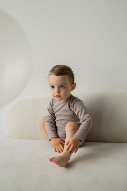 Boy sitting on a couch wearing beige bodysuit