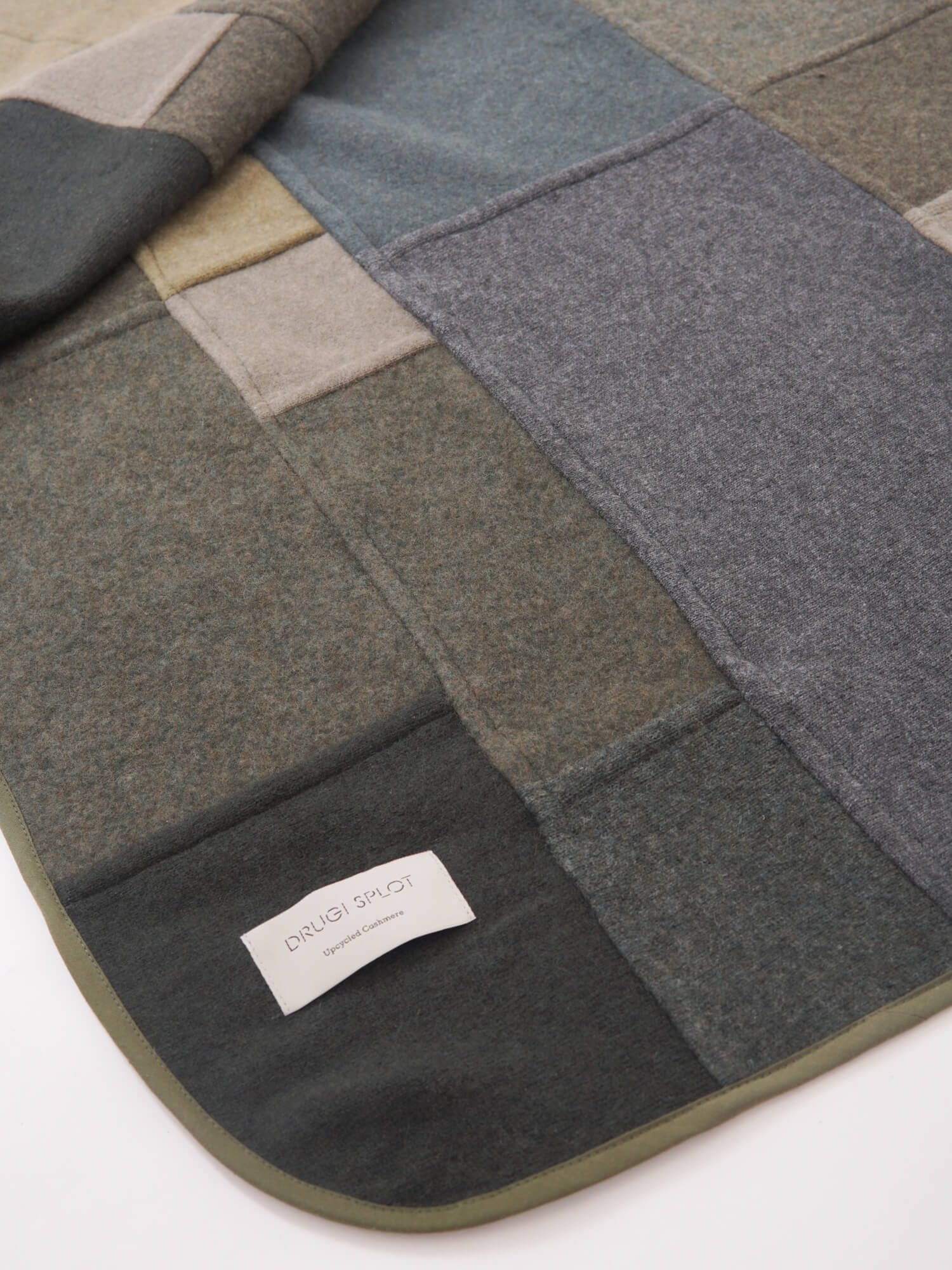 A patchwork blanket with rectangles in shades of grey, green, brown, and beige laid out on a white background.