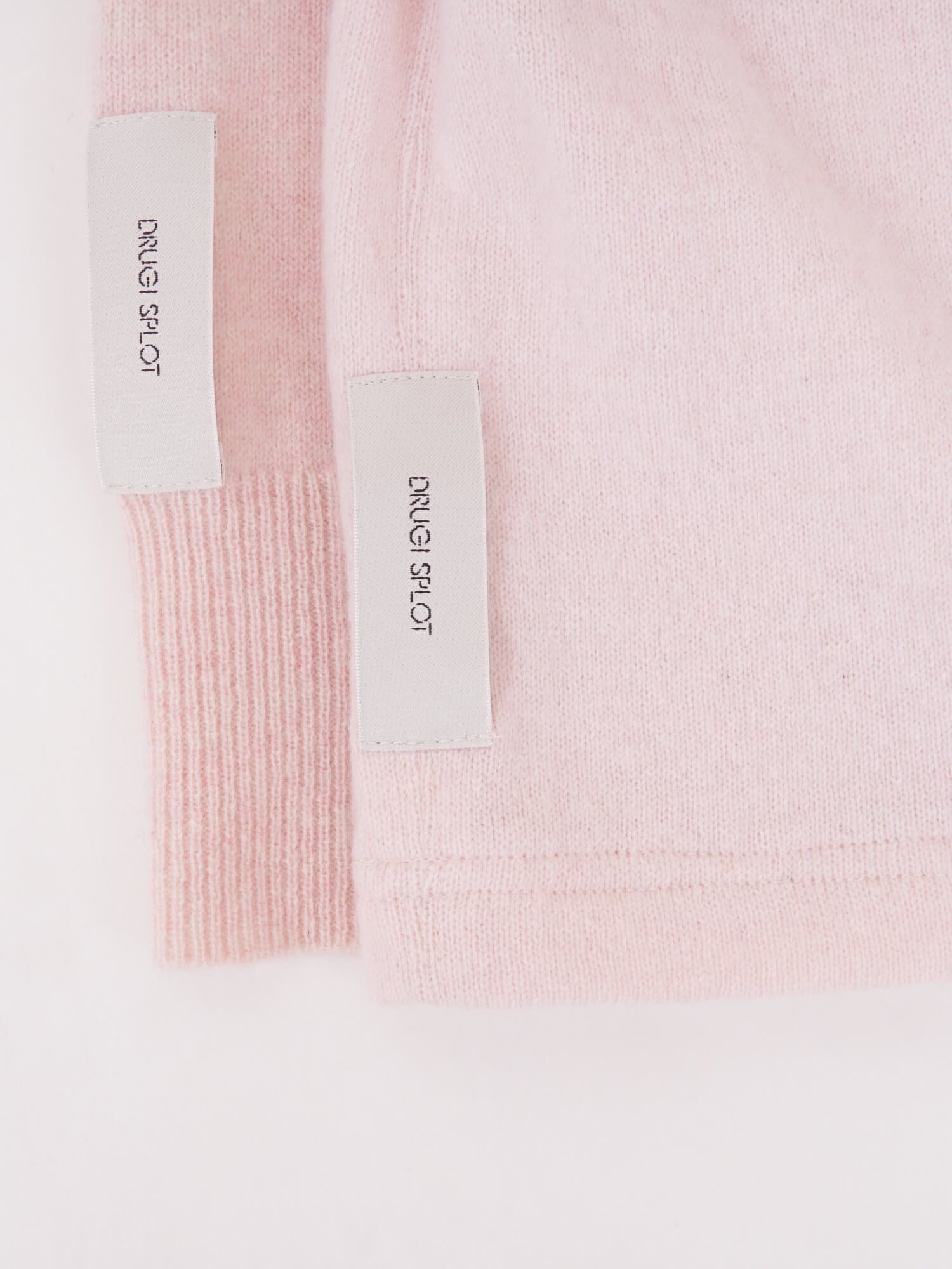 Two folded light pink beanies with small white tags on a plain white background.