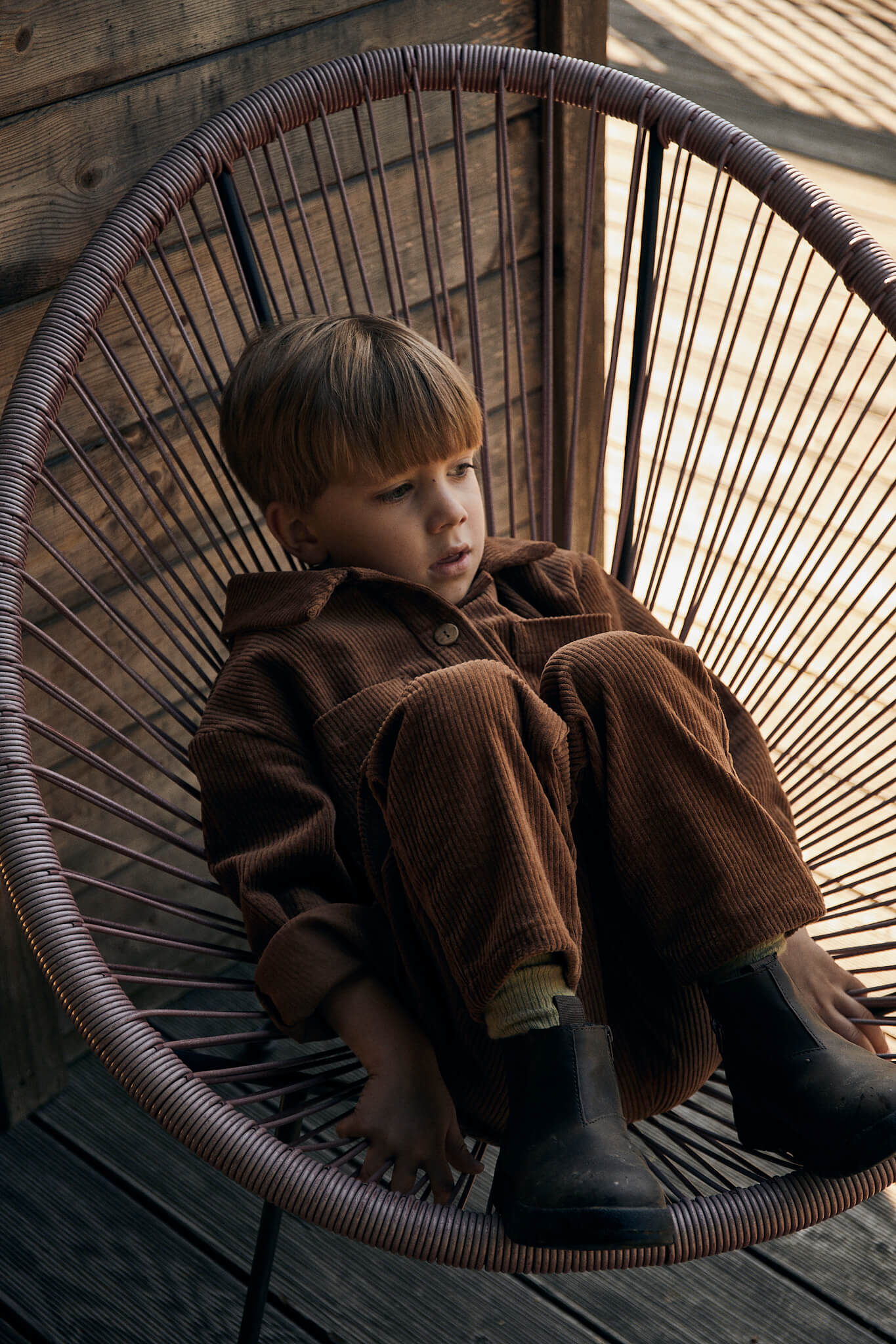 boy wearing brown corduroy set made of jacket and trousers sitting on a chair