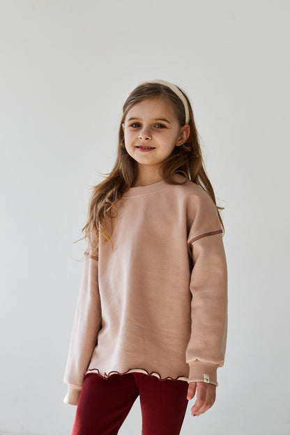 Girl wearing pink sweatshirt and red leggings smiling to the camera on a white background