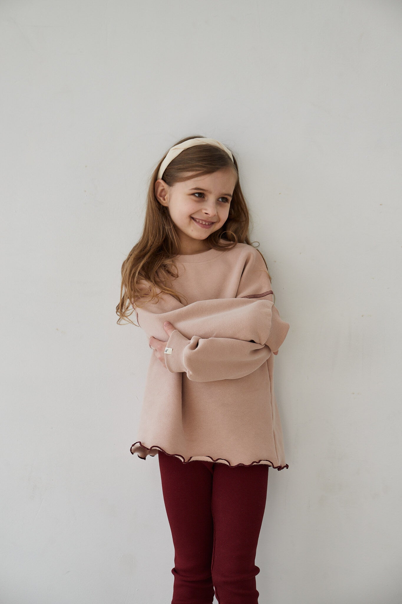 Girl wearing pink sweatshirt and red leggings smiling to the camera on a white background