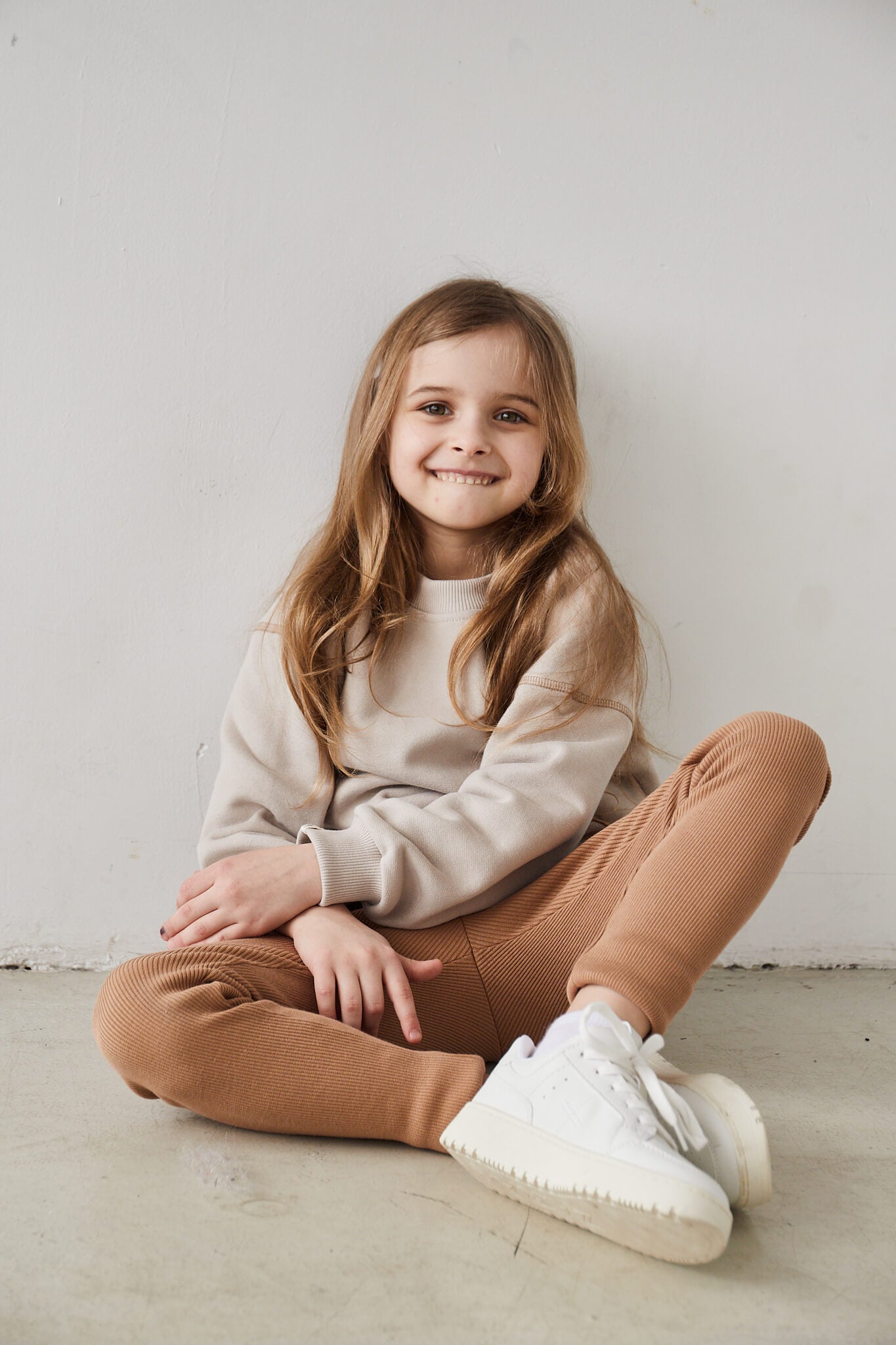 Girl wearing beige sweatshirt and brown leggings on a white background