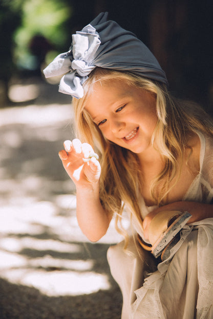 A smiling girl wearing a light blue turban holding her shoes in her hand and looking at a stone in her hand. 