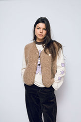 Person wearing a beige vest over a white sweater with star designs on a plain background