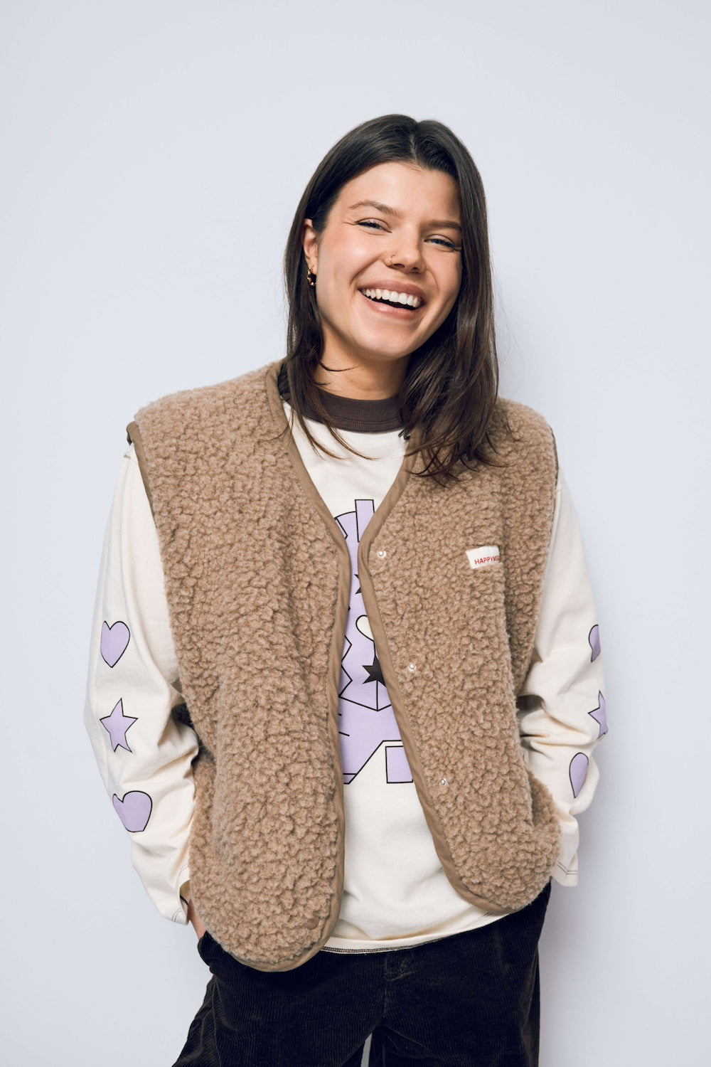 Person wearing a beige vest over a white sweater with purple designs on a light gray background