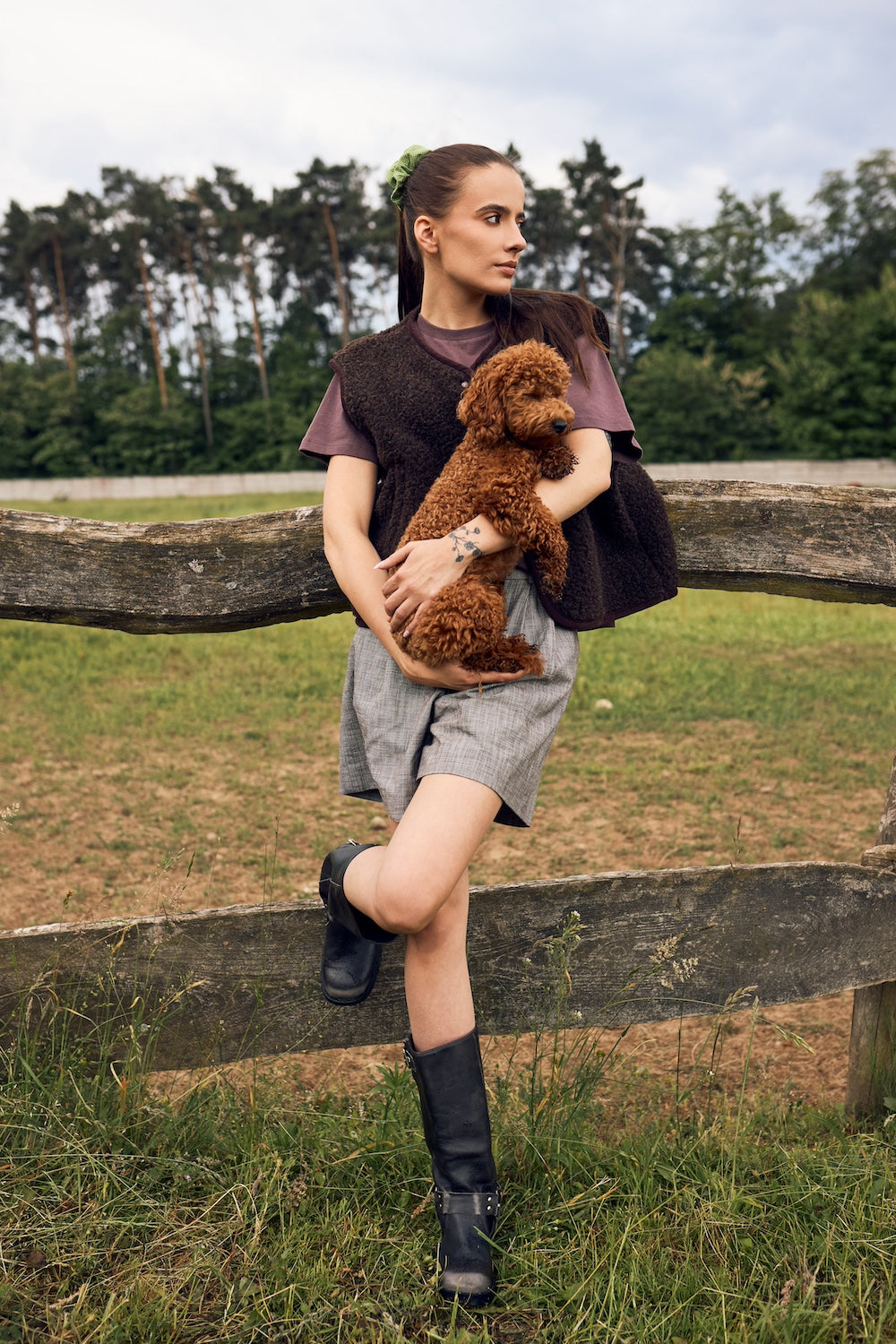 Woman holding a brown dog outdoors near a wooden fence with trees in the background