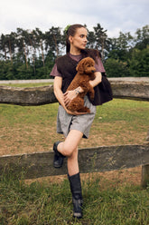 Woman holding a brown dog outdoors near a wooden fence with trees in the background
