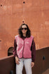 Person wearing a pink vest and sunglasses standing against a rust-colored wall.