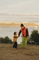 Woman and child holding hands by a lake with mountains in the background