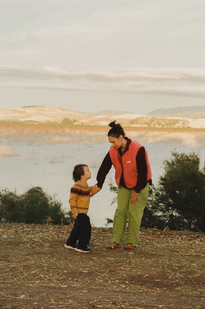 Woman and child holding hands by a lake with mountains in the background