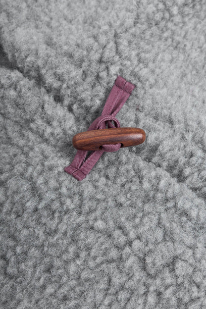 Close-up of a textured gray wool or fleece garment with a single toggle closure featuring a dark brown wooden knob and dusty mauve fabric ties.