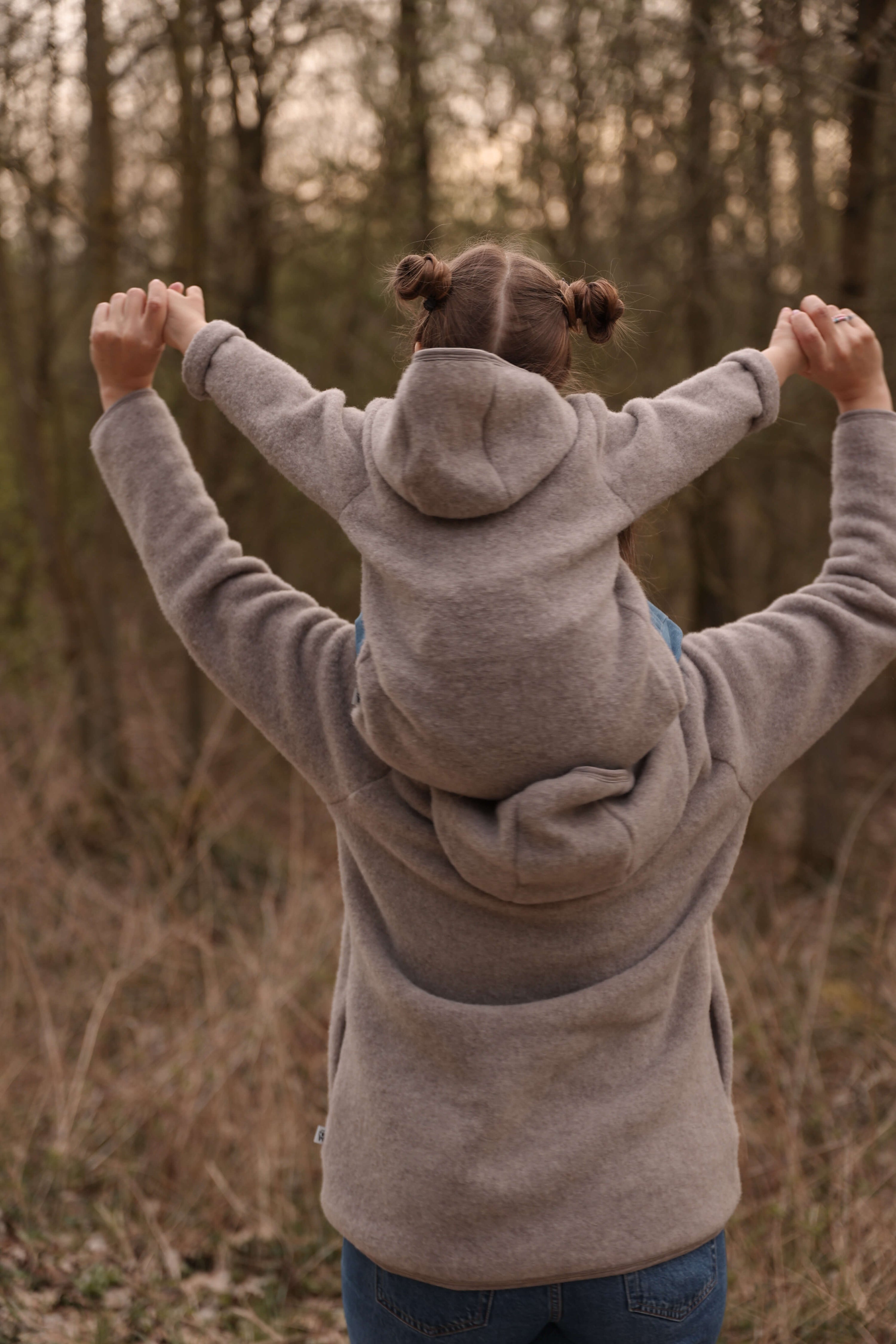 Woman and child wearing matching gray hoodies standing in a forest