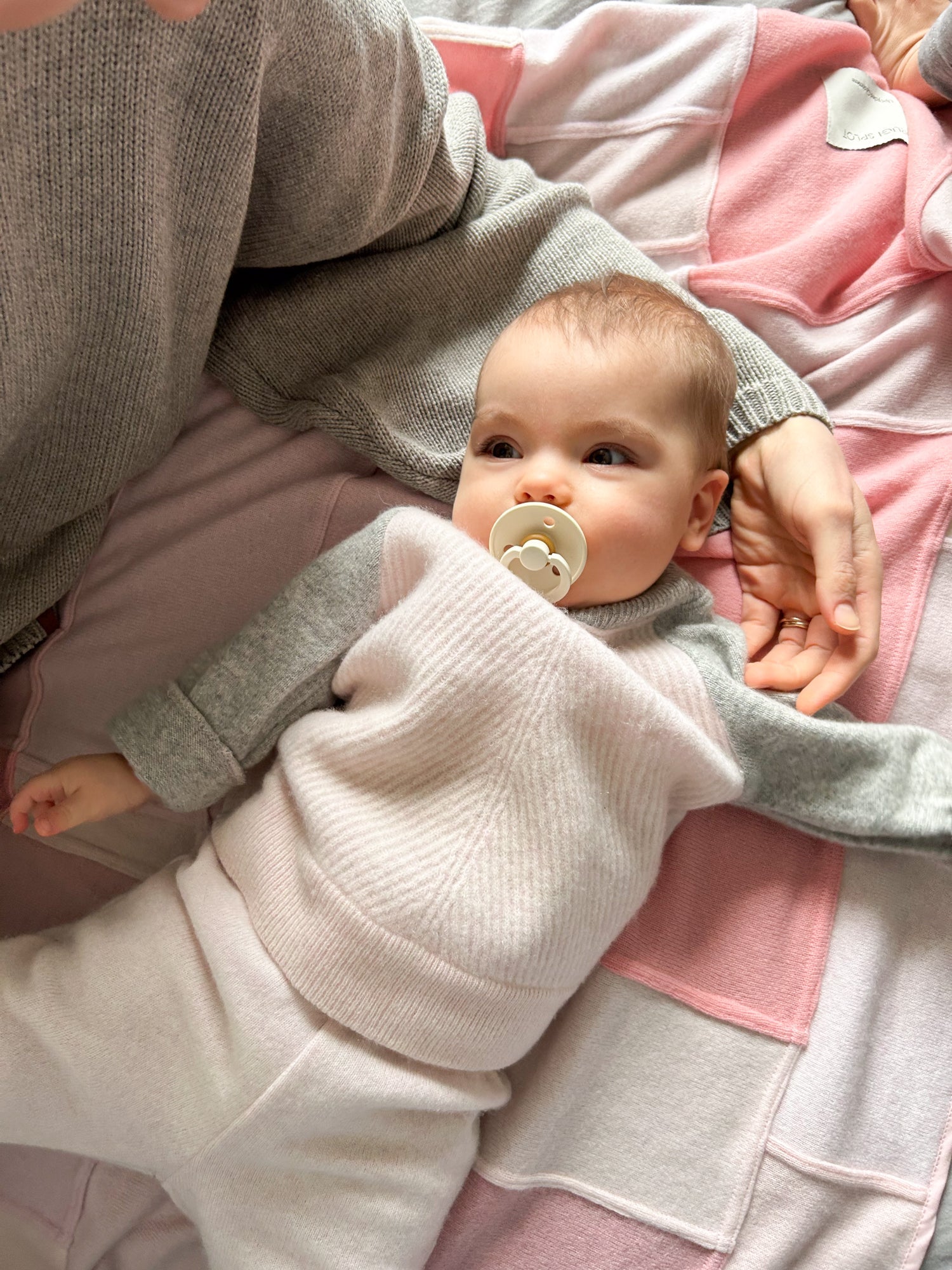 Kleines Baby liegt auf der Rücken auf der Kaschmirdecke in Rosa Farbe, ist angezogen in rosa Kaschmir Set. Das Baby liegt eben der Mutter