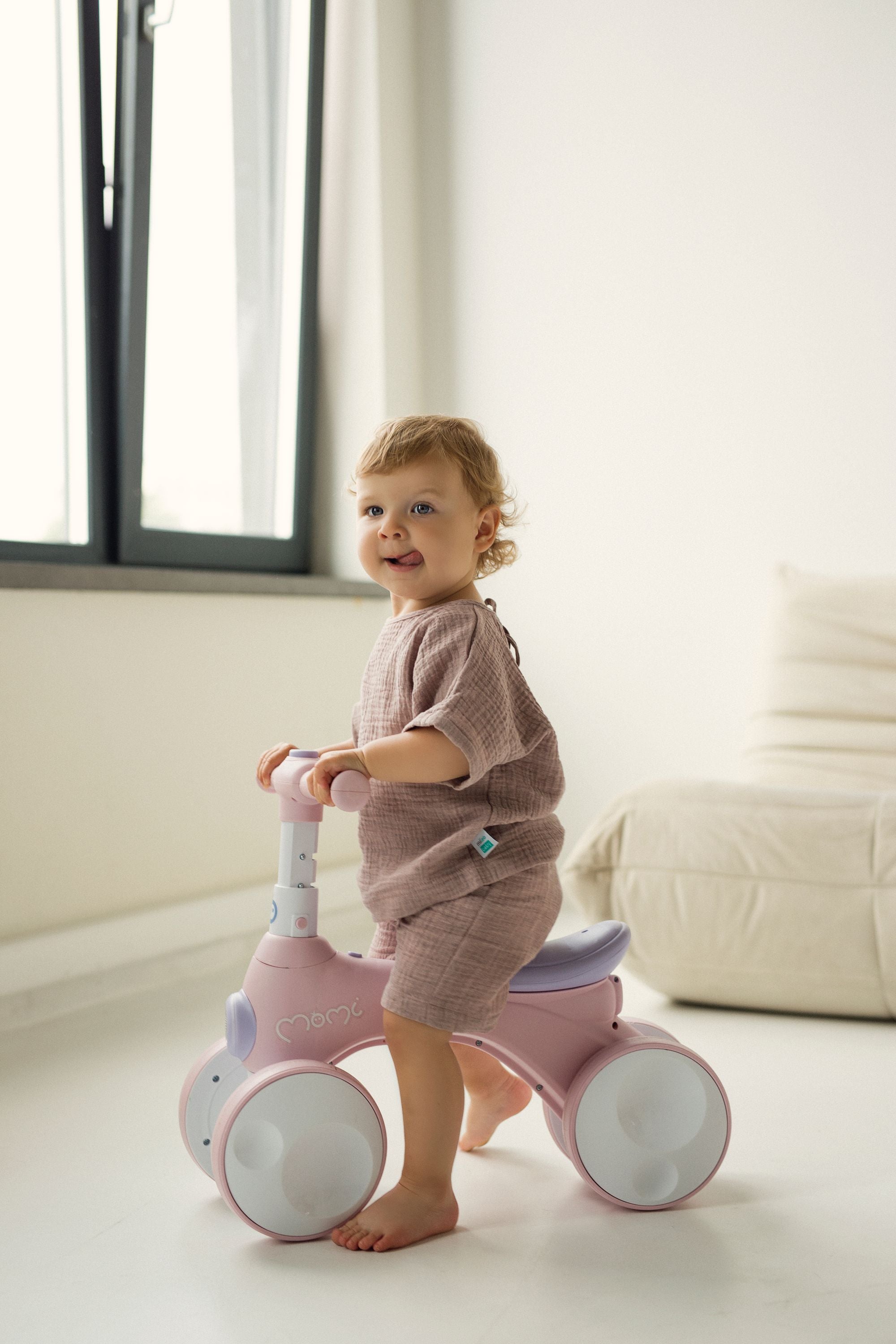 Child playing with a pink balance bike in a bright room wearing pink set