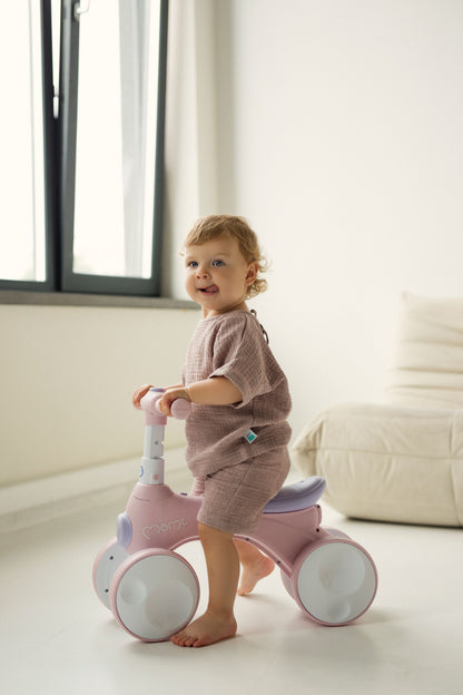 Child playing with a pink balance bike in a bright room wearing pink set