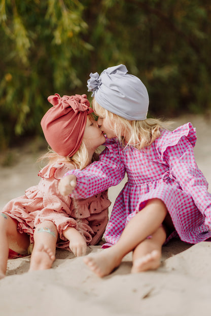 Two sisters, little girls sitting on the beach and giving each other a kiss. They wear cute dresses and adorable turbans