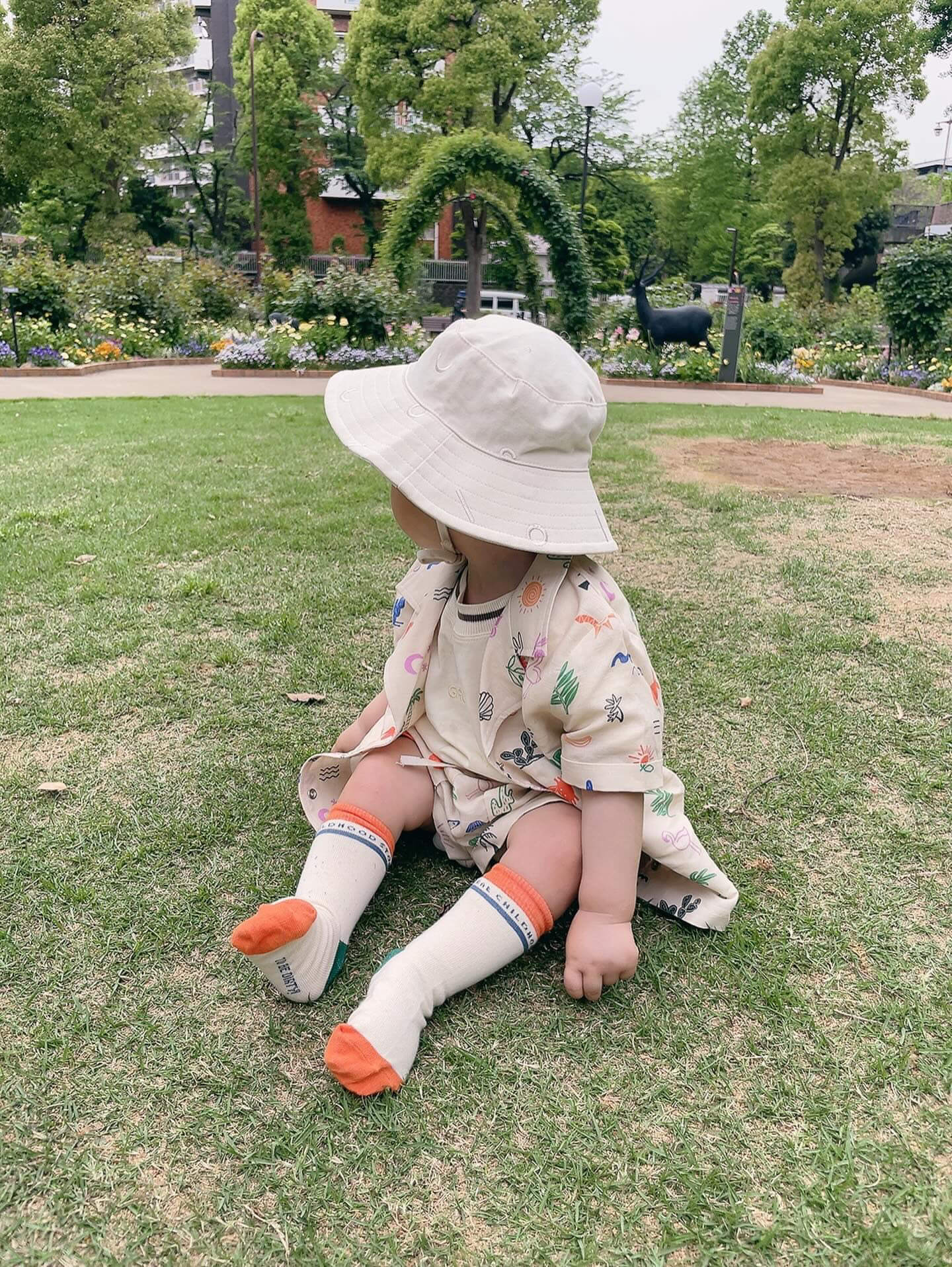 Child sitting on grass wearing a wide-brimmed hat and colorful socks in a park setting.