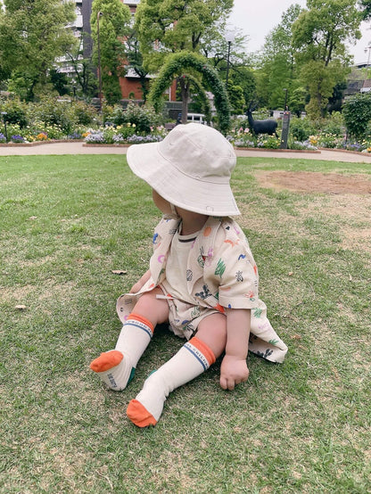 Child sitting on grass wearing a wide-brimmed hat and colorful socks in a park setting.