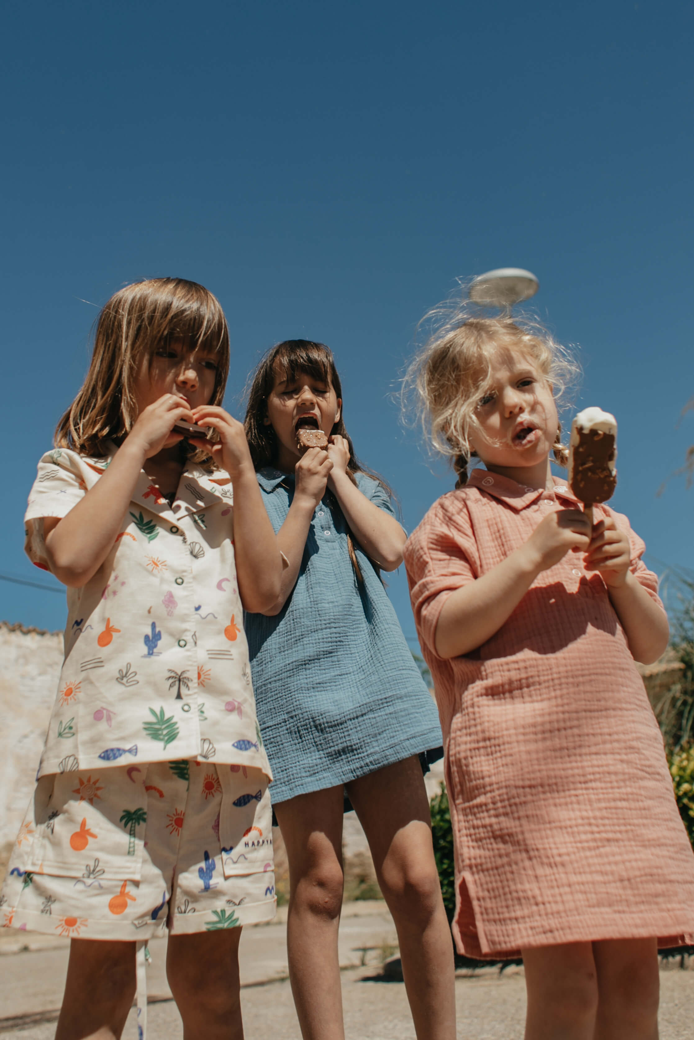 Three children enjoying ice cream against a clear blue sky