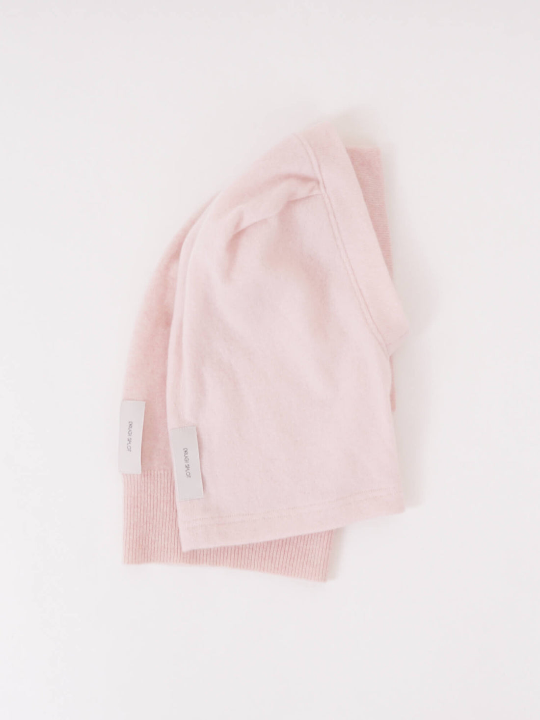 Two folded light pink beanies with small white tags on a plain white background.