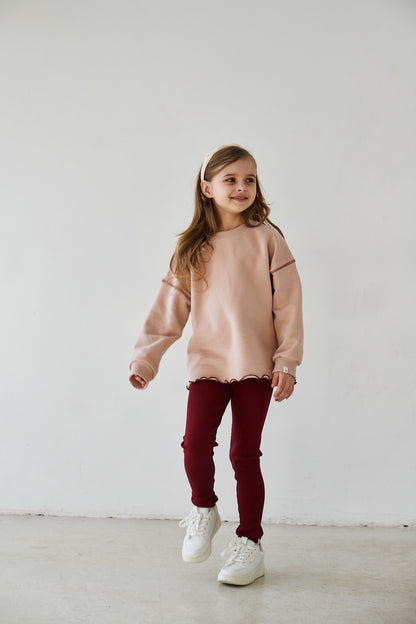 Girl wearing pink sweatshirt and red leggings smiling to the camera on a white background