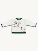 White longsleeve with a round neckline, loose fit, and a decorative contrasting ribbed cuff. It features a red and green print of a dachshund on the front.