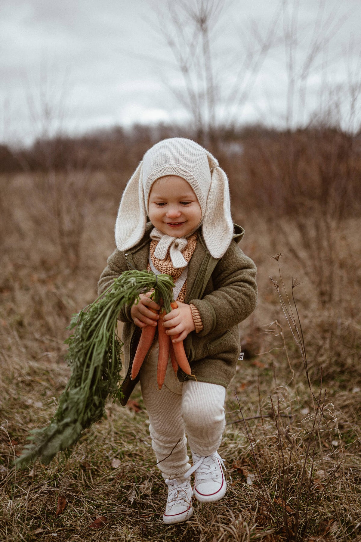Child in a field wearing a bunny outfit holding carrots