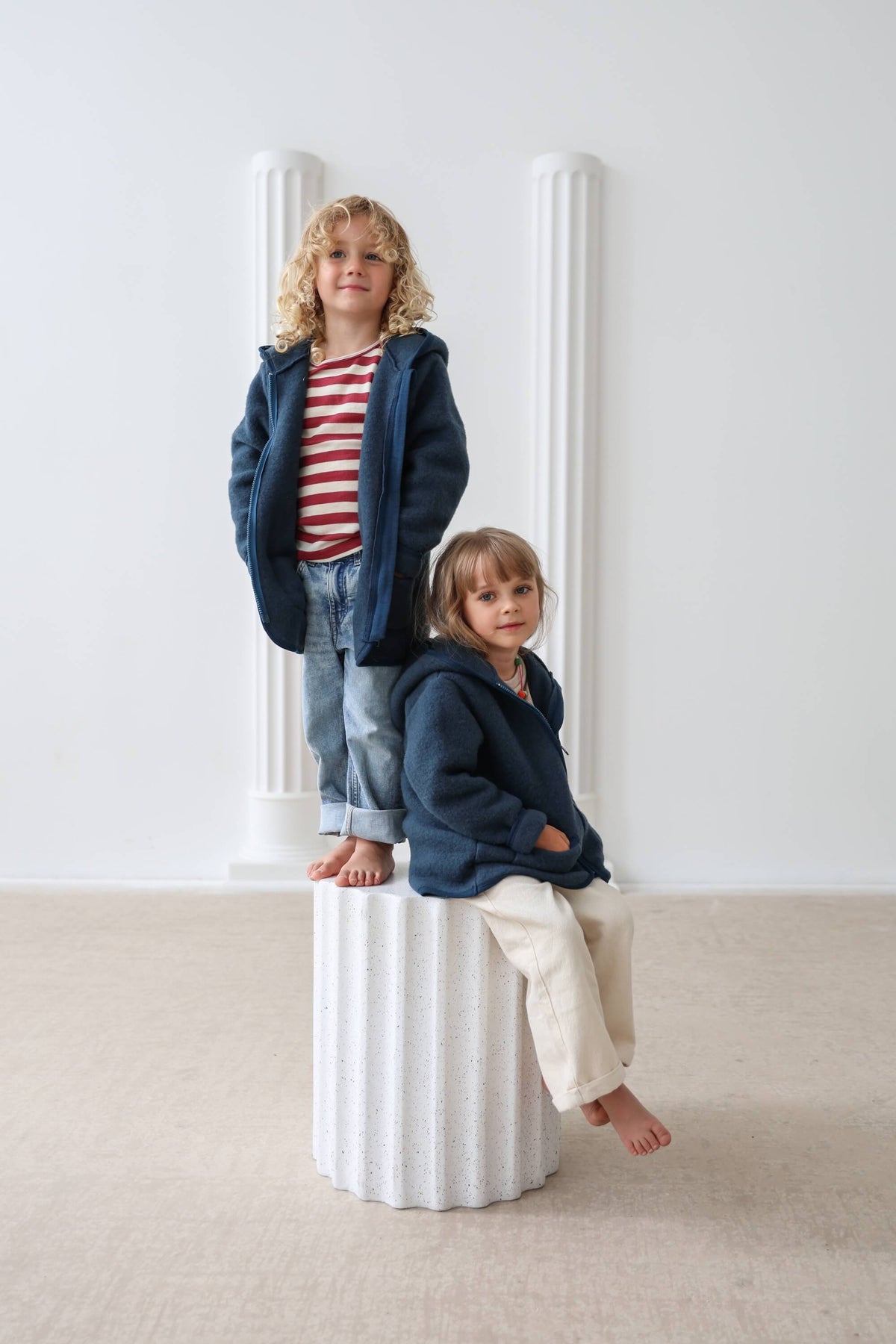 Two children wearing matching navy blue hoodies in a minimalistic setting