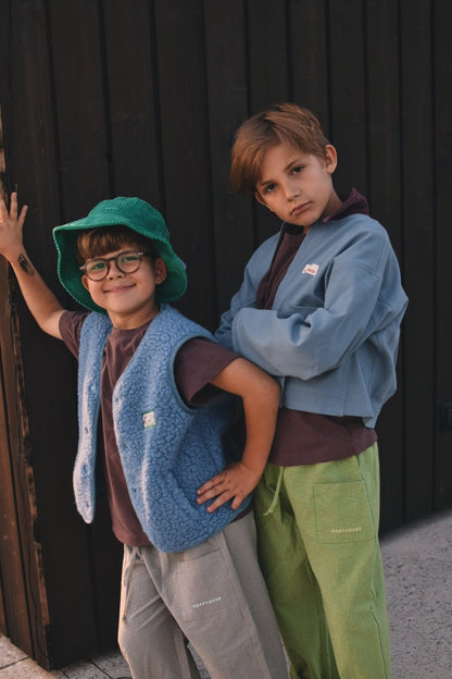 Child in blue fleece vest and green hat outdoors
