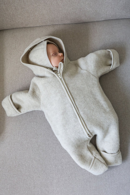Baby in a ivory onesie lying on a gray surface
