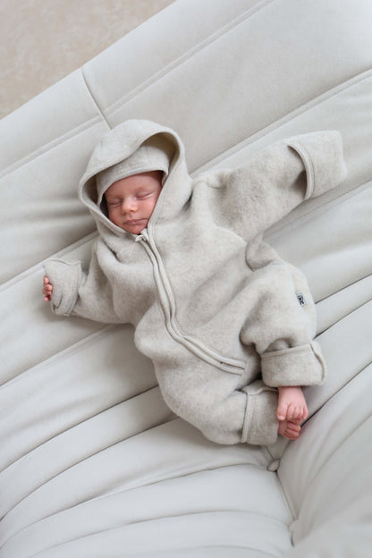Newborn baby in an ivory hooded outfit lying on a white cushion