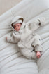 Newborn baby in an ivory hooded outfit lying on a white cushion
