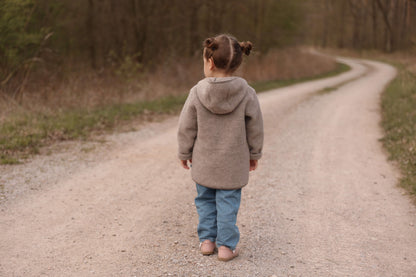 Child wearing a taupe merino fleece jacket on a forest path