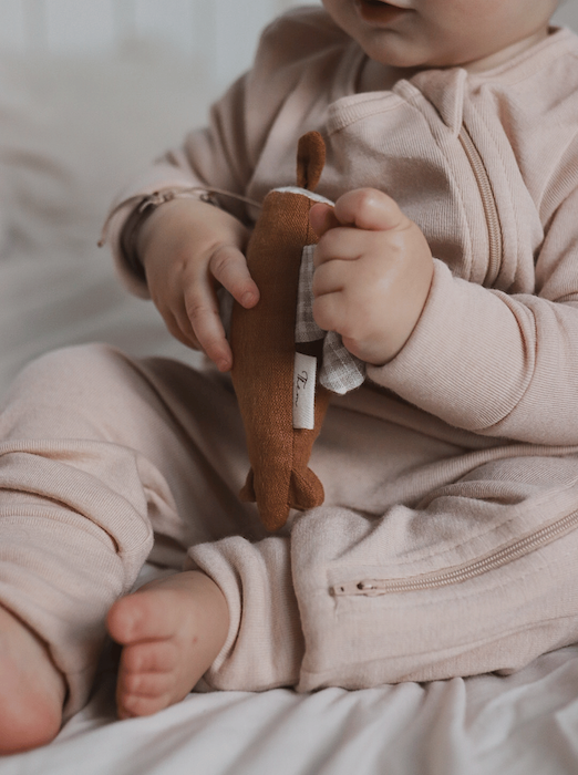 sitting baby wearing a beige merino wool and silk overall holding a brown toy