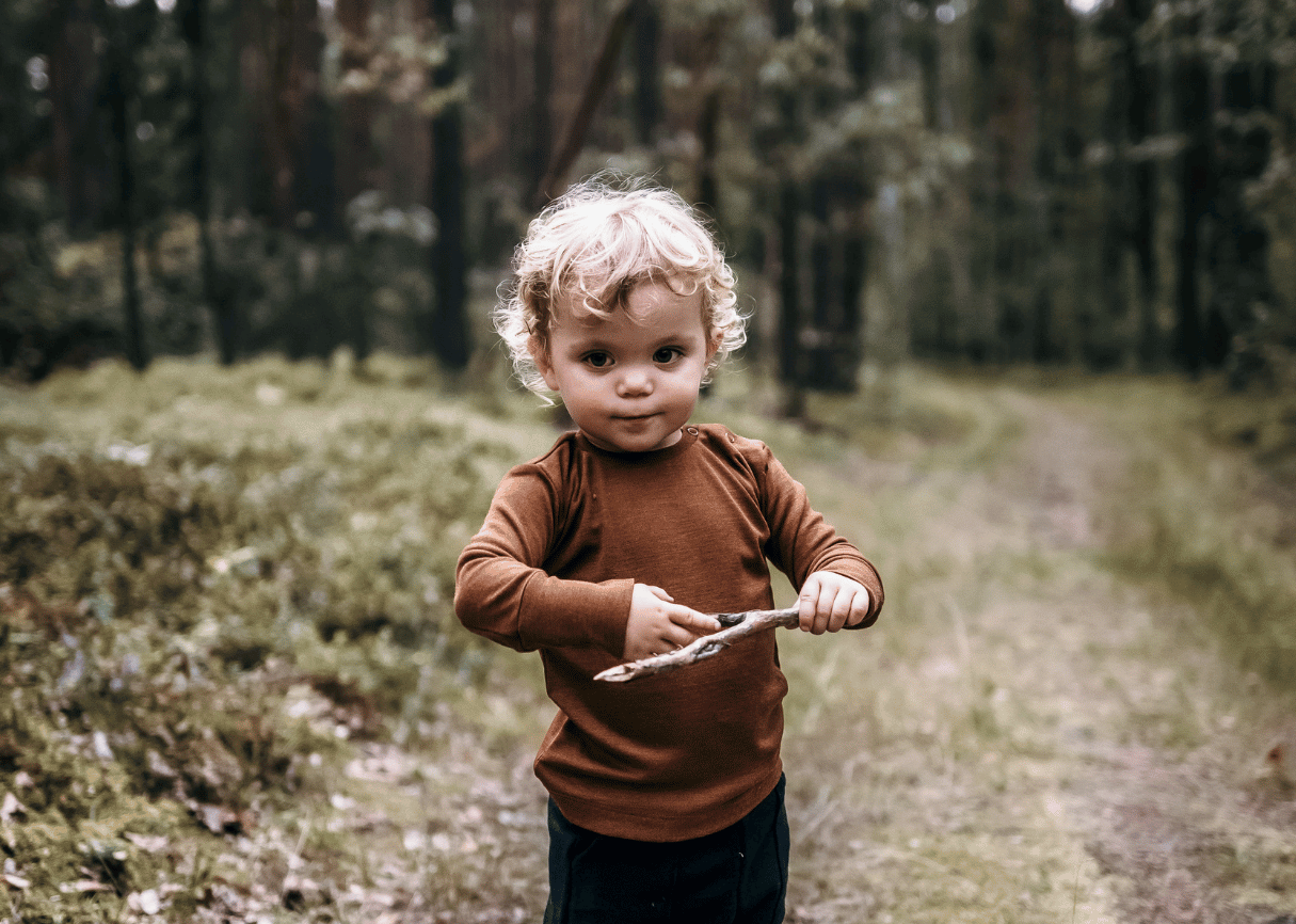 small boy in a forest wearing brown merino wool and silk tshirt