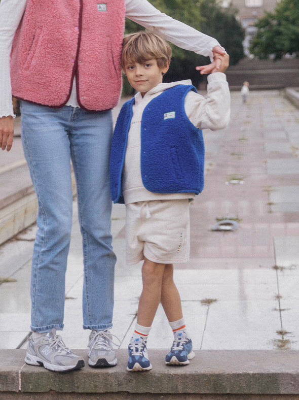 Adult and child wearing merino wool vests standing outdoors on a stone pathway.